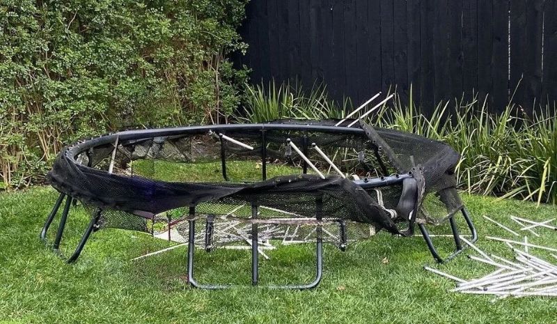 An old trampoline being disassembled for removal in a backyard