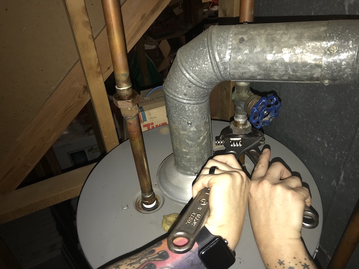 Two hands using two wrenches to disconnect cold water supply from old water heater
