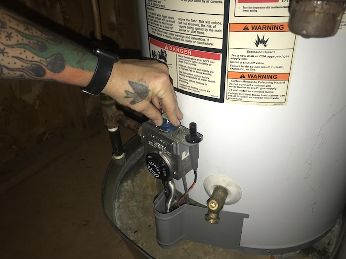 Hand turning water heater to off position.