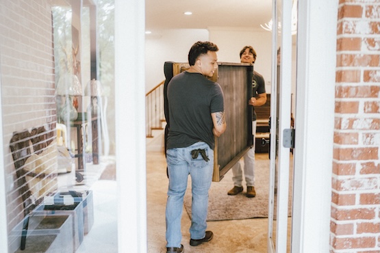 Two furniture removal and assembly pros carrying out an old piece of furniture for a customer