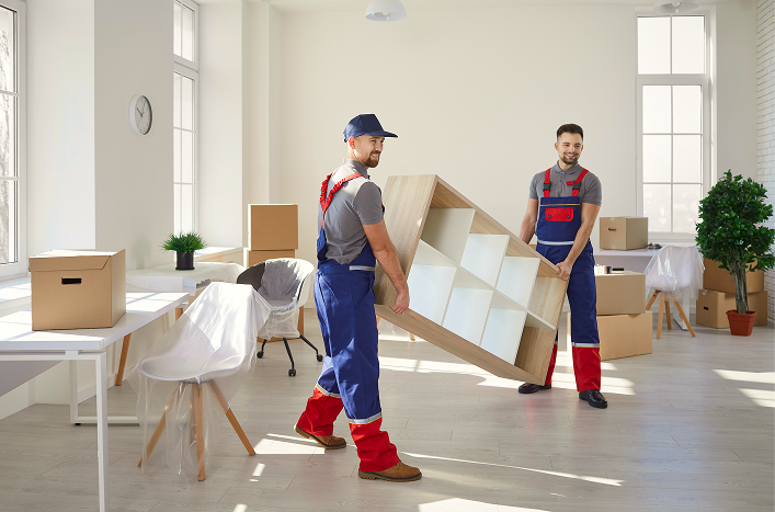 Two junk removal pros carrying old furniture out of an office for a business client